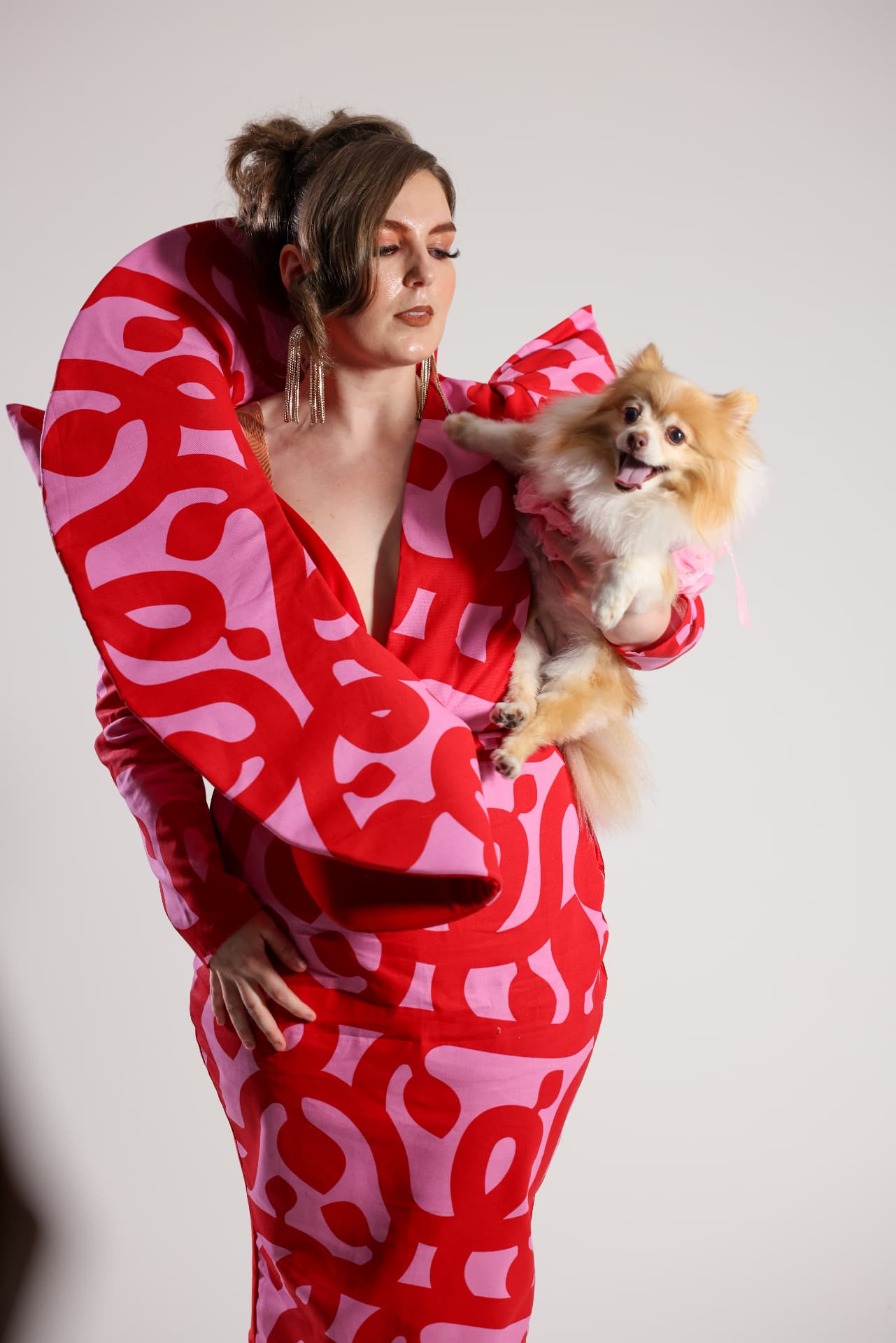 Model in a red and pink printed gown holding a pomeranian